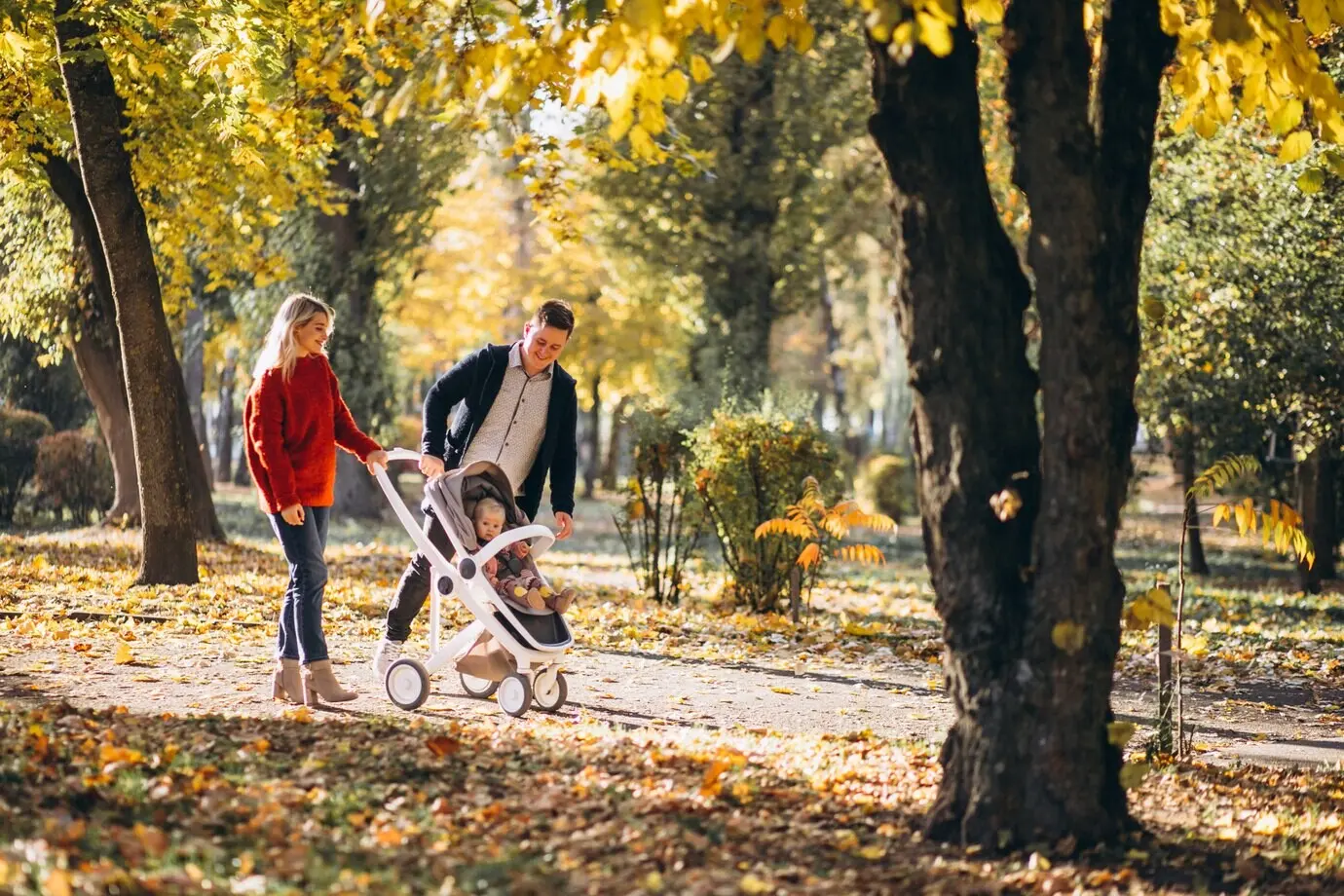 Familia con su hija bebé en un cochecito caminando por un parque otoñal.