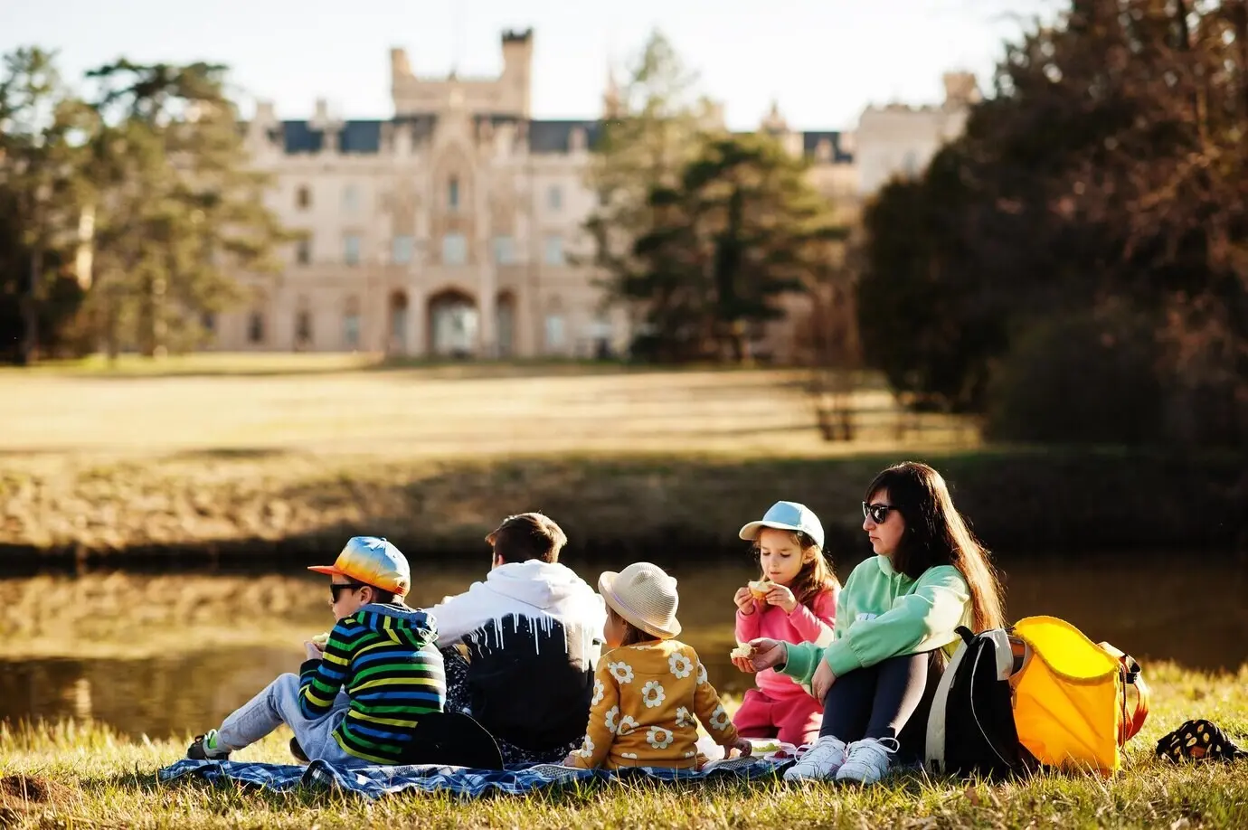 Madre con cuatro niños haciendo un picnic cerca de un estanque del parque de Lednice, con un castillo de fondo, en la República Checa.